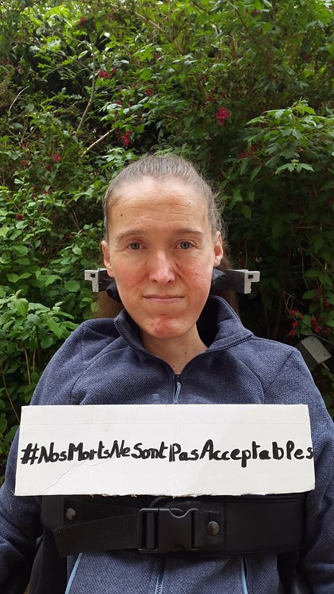 Femme en fauteuil roulant, tenant un panneau avec inscrit "#NosMortsNeSontPasAcceptables"